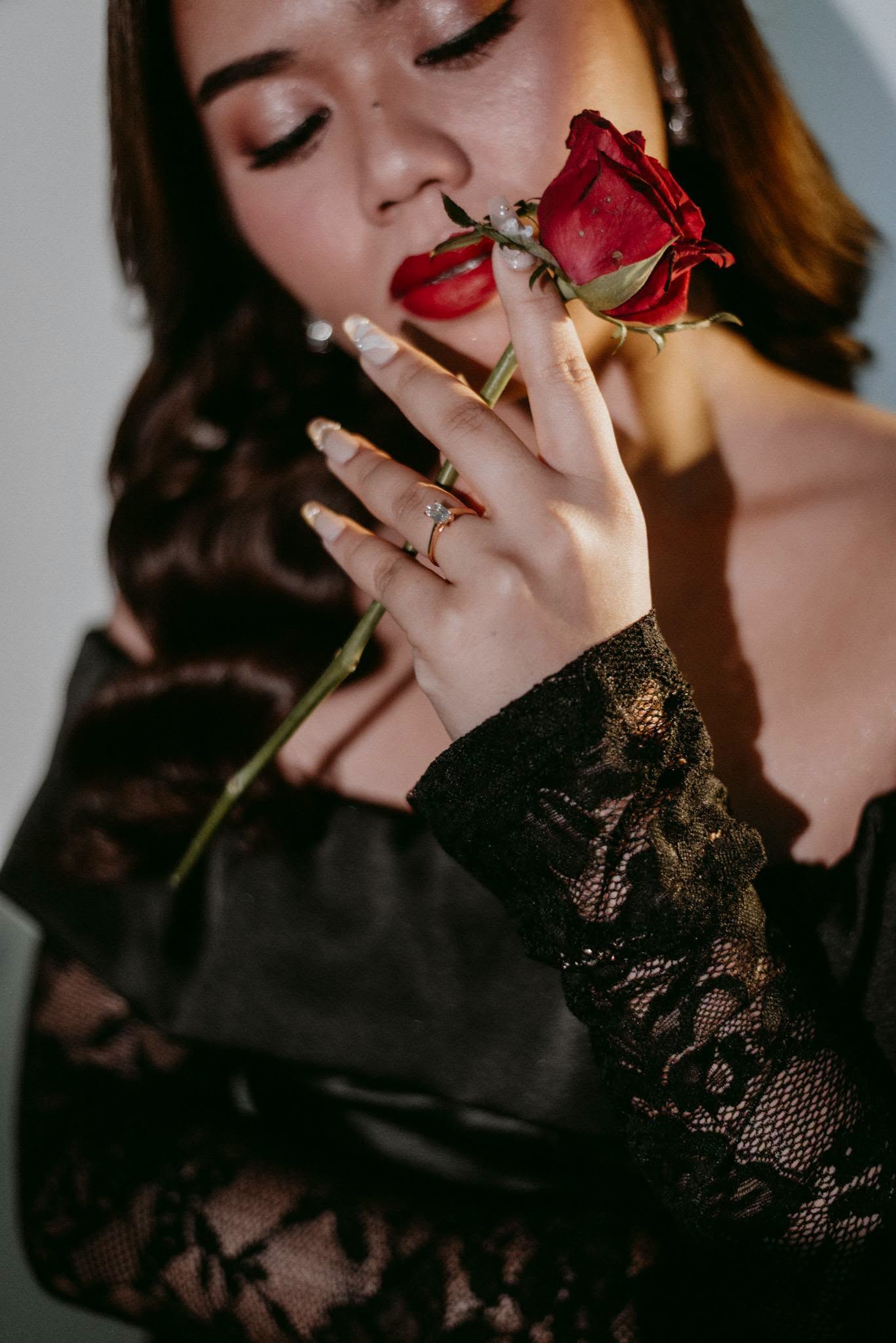 Model wearing gold rings, holding a red rose